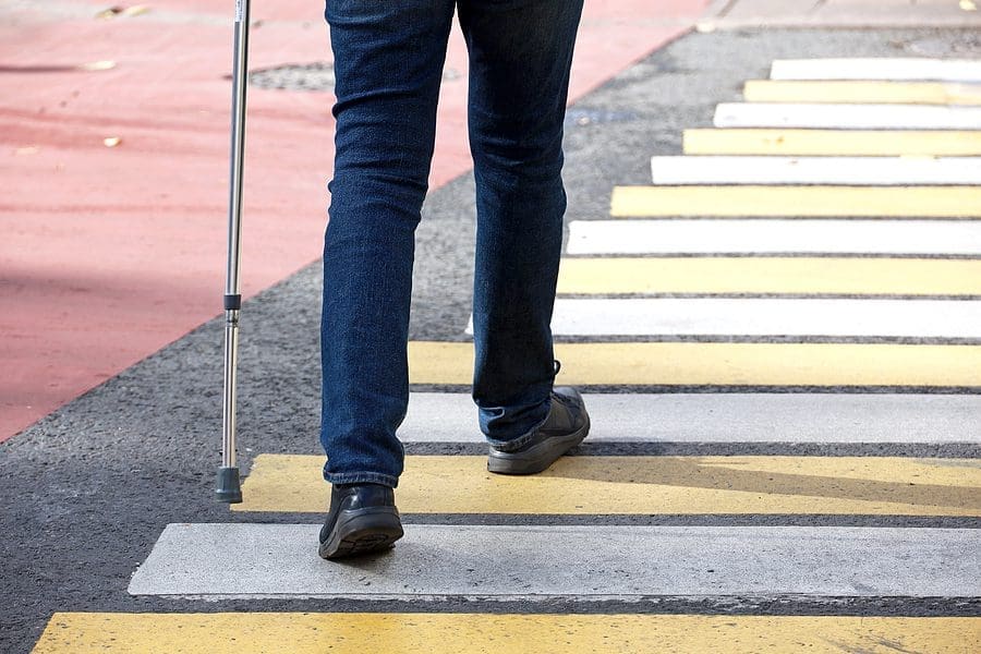 Man Walking With A Cane On Crosswalk. Male Legs In Jeans On Pede