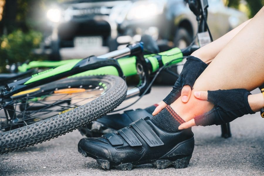 Injured cyclist holds their ankle after a bicycle accident involving a car and a pedestrian
