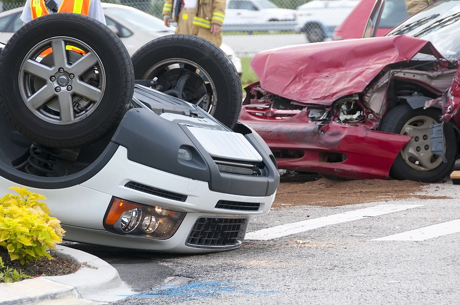 two cars, one overturned car and a red car with crushed hood after one of the major types of motor vehicle accidents