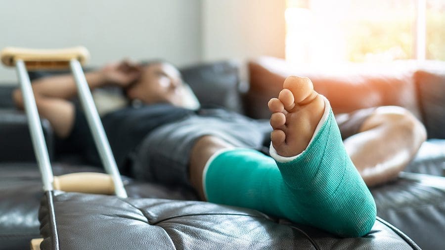 Young man lies on the couch with his leg in a cast and crutches propped up to the side