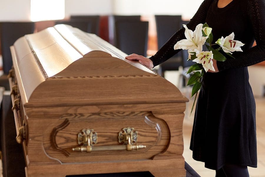 Woman holding white flowers placing her hand on a casket at a funeral