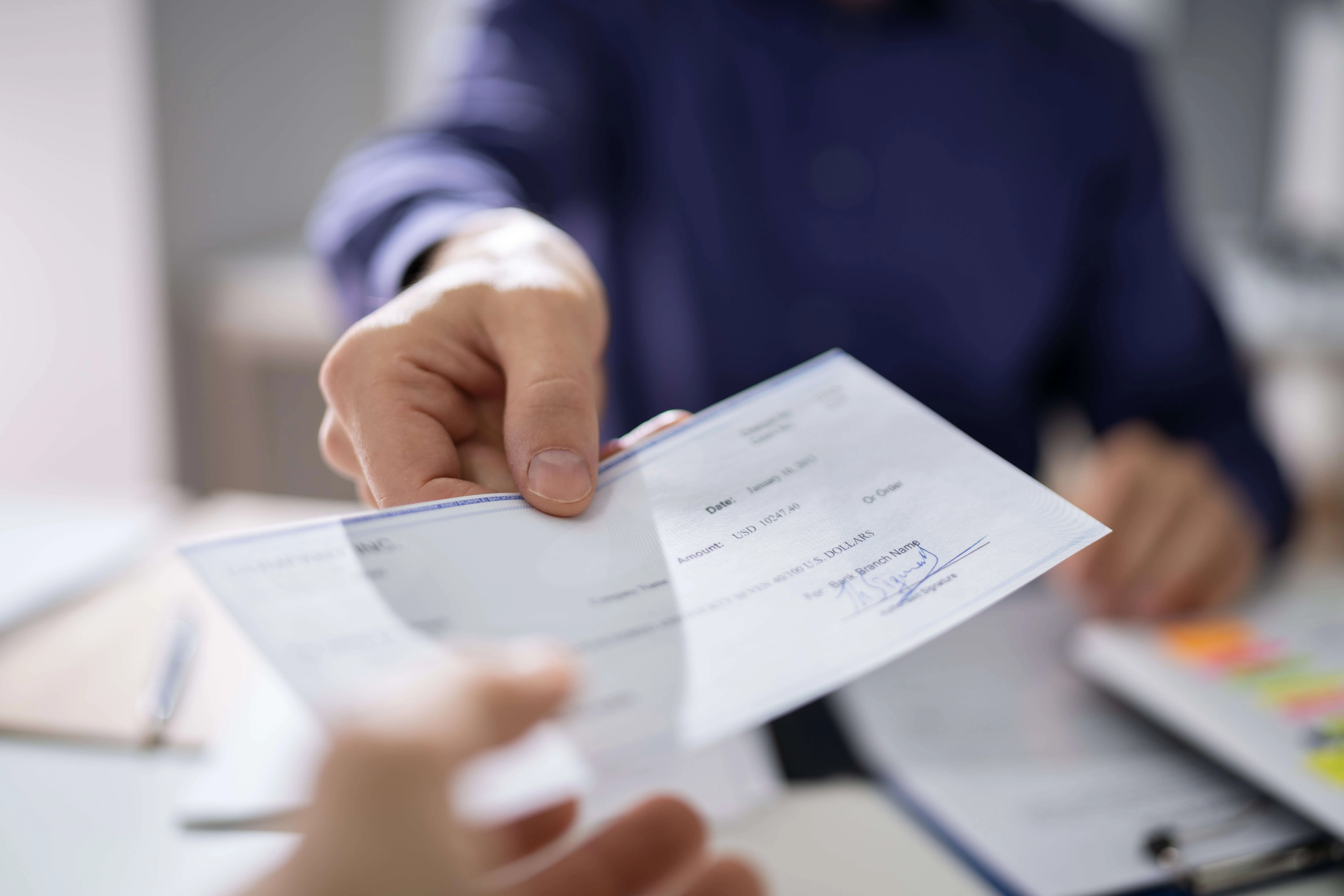 Person in business suit handing another person a settlement check for their car accident claim