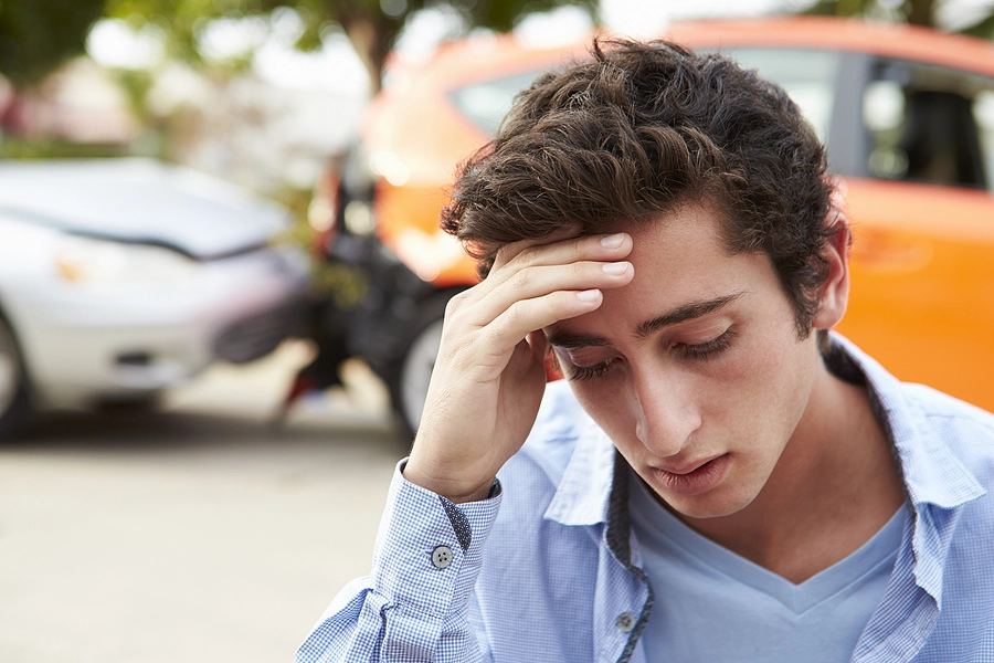 New teen driver stands in front of a car accident he caused looking worried